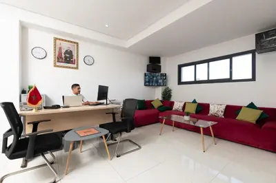 a man sitting at a desk in a living room with a red couch at Garden Bay Signature AppartHotel in Casablanca