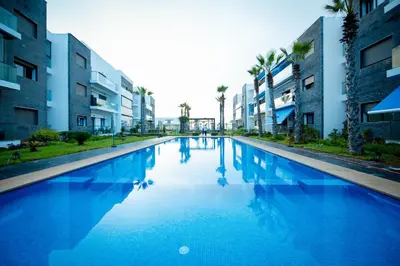 a large blue swimming pool with palm trees and buildings at Garden Bay Signature AppartHotel in Casablanca