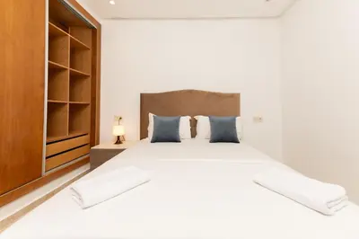 a white bedroom with a large bed and a cabinet at Garden Bay Signature AppartHotel in Casablanca