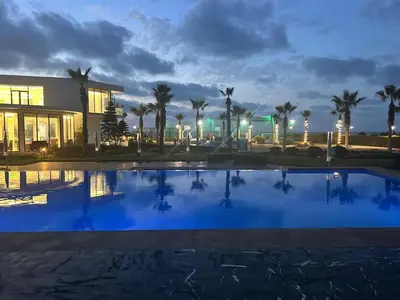 a pool in front of a building with palm trees at Garden Bay Luxe, Tamaris Bord de Mer in Casablanca