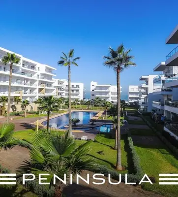 a resort with a pool and palm trees and buildings at Peninsula Bay in Dar Bouazza