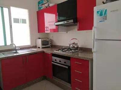 a kitchen with red cabinets and a white refrigerator at Superbe appartement en résidence avec piscine in Mohammedia