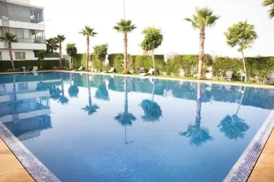 a large swimming pool with palm trees and a building at KST Home-Heaven Beach Sidi Rahal in Sidi Rahal