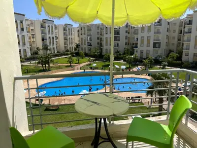 a balcony with a table and chairs and a swimming pool at Beautiful 2 bedrooms apartment in Bouznika in Bouznika