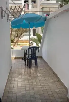 a patio with two chairs and a blue umbrella at Apparemment sur mer avec piscine al Mansouria in O Ben Slimane