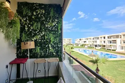 a balcony with stools and a green wall with a pool at Appartement Balneaire avec piscine à El Mansouria in Mansouria