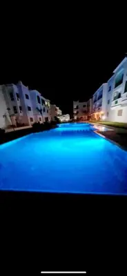 a large blue swimming pool at night with buildings at appartement avec piscines in Mansouria