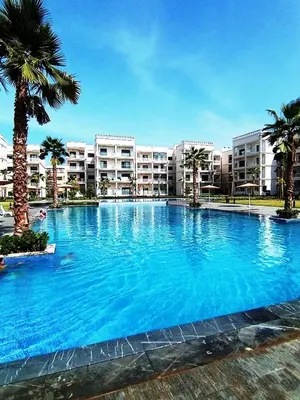 a large swimming pool with palm trees and buildings at Charming appartement in Bouznika in Bouznika