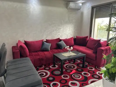 a living room with a red couch and a table at Belle Appt vue sur Piscine à Bouznika plage in Bouznika