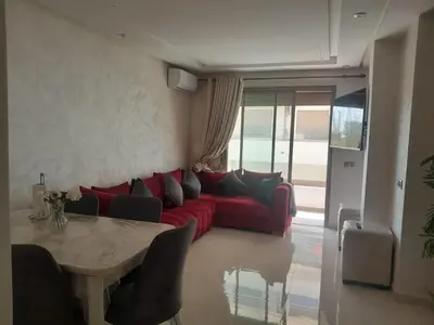 a living room with a red couch and a table at Belle Appt vue sur Piscine à Bouznika plage in Bouznika