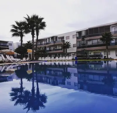 a swimming pool with chairs and palm trees and a building at Appt moderne 3 chbr Blanca Beach in Sidi Rahal