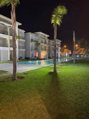 a large building with palm trees in front of a pool at Appartement casa bay sidi rahel in Sidi Rahal