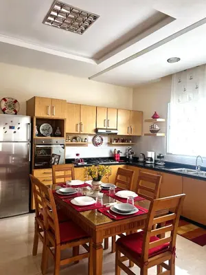a kitchen with a wooden table with chairs and a refrigerator at Villa près de la mer, sidi rahal route de dar bouazza in Bir Jedíd Saint-Hubert