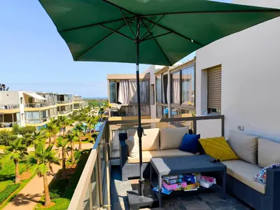 a balcony with a green umbrella and a couch at Les Sables de Sidi Rahal - Blue Beach in Sidi Rahal
