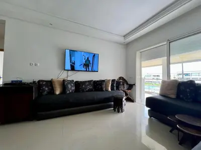 a living room with a couch and a tv on the wall at OlaBlanca2, appartement avec terrasse et vue sur piscine in Sidi Rahal