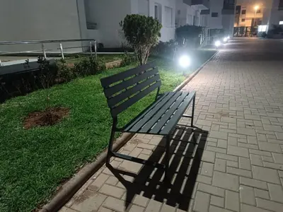 a park bench sitting on the side of a street at night at Sunny 2-Bedroom Apartment with Pool for a Great Stay in Mohammedia