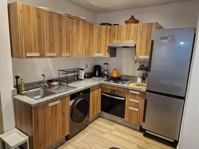 a kitchen with wooden cabinets and a stainless steel refrigerator at Résidence blue beach Sidi rahal in Sidi Rahal