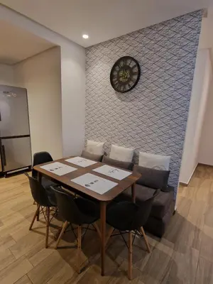 a dining room with a table and a clock on a wall at Résidence blue beach Sidi rahal in Sidi Rahal