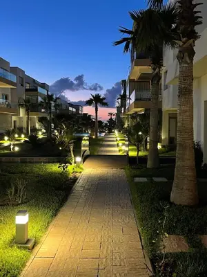 a walkway with palm trees and buildings at night at Résidence blue beach Sidi rahal in Sidi Rahal