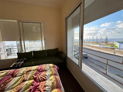 a bedroom with a couch and a large window at Beach flat with pool at Al Mansouria in O Ben Slimane