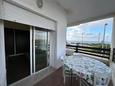 a balcony with a table and a view of the ocean at Beach flat with pool at Al Mansouria in O Ben Slimane