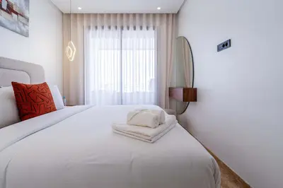 a bedroom with a large white bed with a window at Appartement avec Piscine dans Résidence Privée in Dar Bouazza