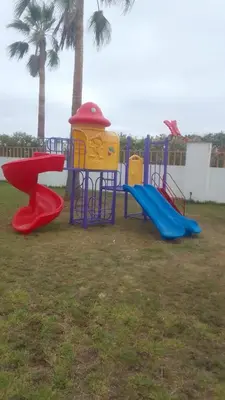 a playground with three slides in a yard with palm trees at Jumeirah in Sidi Rahal
