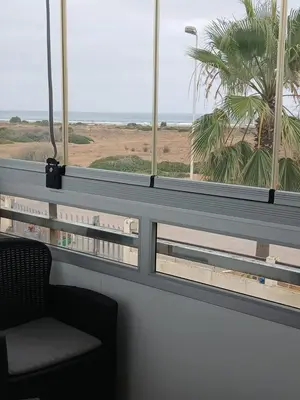 a room with a window with a chair and a palm tree at Appartement BAHIA BEACH piscine plage privée in Bouznika