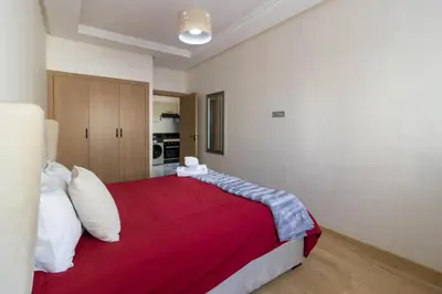 a bedroom with a large bed with red blanket at Studio chic et paisible avec piscine parc et plage in Aïn Harrouda