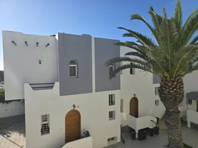 a palm tree stands in front of a white building at Seaside Artist's Villa in Temara