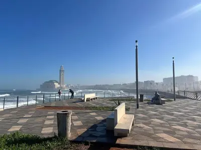 people sitting on benches on a sidewalk near the beach at Le yacht luxury apartment 2BR 2BA corniche with parking in Casablanca