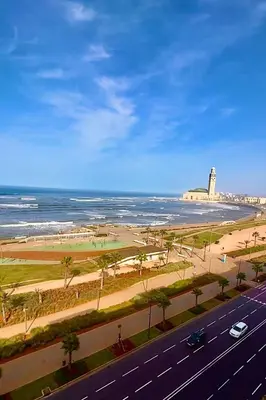 a road next to a beach with a lighthouse and the ocean at Le yacht luxury apartment 2BR 2BA corniche with parking in Casablanca