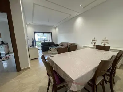 a dining room and living room with a table and chairs at Appartement Luxe Vue Piscine Résidence Les Perles de Bentriaa, El Mansouria in Mohammedia