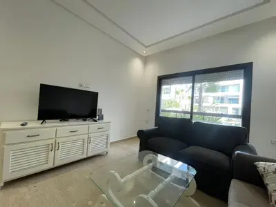 a living room with a couch and a flat screen tv at Appartement Luxe Vue Piscine Résidence Les Perles de Bentriaa, El Mansouria in Mohammedia