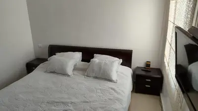 a white bed with white pillows and a night stand at Résidence balnéaire casablanca in Dar el Maïzi