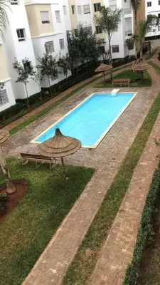 an empty swimming pool with a table and an umbrella at Détente et confort en face de mer in Casablanca