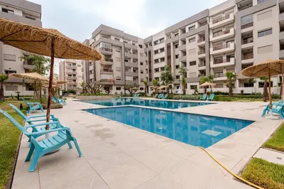 a swimming pool with blue chairs and umbrellas at 5 min from airport, 1 bedroom, balcony, pools in Nouaceur
