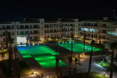 a building with green lights in a courtyard at night at Résidence luxueuse avec 5 Piscine A MANSOURIA près de la Mer in O Ben Slimane