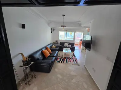 a living room with a black leather couch and a tv at Appartement cosy au centre de casablanca in Casablanca