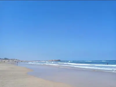 a beach with the ocean and people in the water at Ocean park , for married couples and families only , Luxury fully furnished one bedroom flat next to zenata beach with five avialable swimming pool at the compound in Casablanca