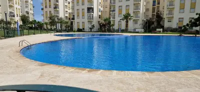 a large blue swimming pool in front of some buildings at Appartement avec piscine Bouznika in Bouznika