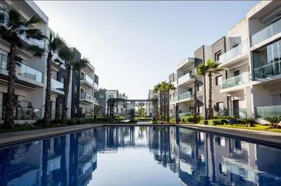 a swimming pool with palm trees and buildings at Appartement Moderne très bien équipé pour familles seulement- Résidence Garden Bay Dar Bouazza in Tamaris
