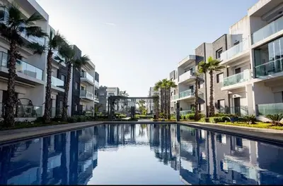 a swimming pool in front of a building with palm trees at Appartement Moderne très bien équipé pour familles seulement- Résidence Garden Bay Dar Bouazza in Tamaris