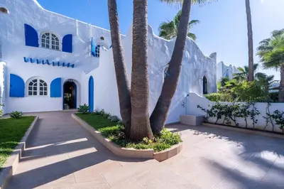 a white building with palm trees in front of it at Villa in Golf Resort with Shared Pool in Bouznika
