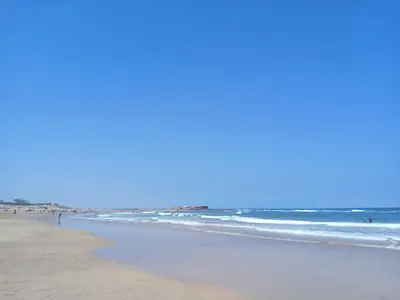 a beach with the ocean and people in the water at Studio Cosy avec Mezzanine Piscine et Plage à 5 min à Zenata City in Aïn Harrouda