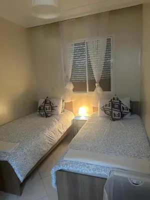 a bedroom with two beds and a lamp in it at Apprt 2min de la Gare,Wi-Fi Fibre, Netflix ,PS4 in Settat