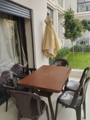a wooden table and chairs on a patio with a window at Appartement à louer à Bouznika avec piscine in Bouznika