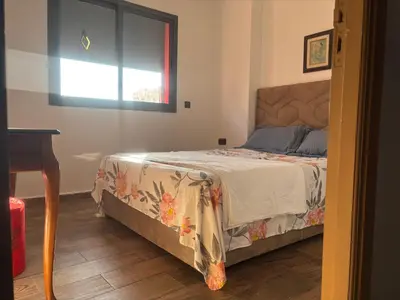 a bedroom with a bed and a table and a window at Cozy apartment near the airport in Deroua