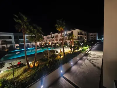 a view of a pool at night with palm trees and buildings at Luxury apartment in Oulad Mbark
