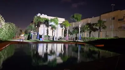 a building with palm trees and a reflecting pool at night at Bel Appart dans une résidence balneaire in Tamaris